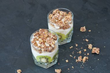 Yunan yoğurdu, granola, muz ve kivi. Koyu arka planda cam bardak tatlılar, kopya alanı. Konsept vücut ve sağlıklı gıda