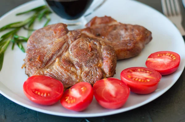 Fragrant pork meat steaks with spices, tomatoes and sauce, on a gray plate, on a dark concrete background, close-up — Stock Photo, Image