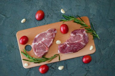 Düz yatıyordu, çiğ et iki domuz bifteği domatesli sarımsak ve biberiyeli ahşap kesim tahtasına yakın çekim.