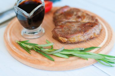 Pişmiş, ahşap bir tahtanın üzerinde ızgara domuz eti, soya sosu, biberiye ve domates, açık arkaplanda.