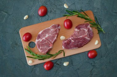 Domatesli çiğ domuz bifteği, sarımsak ve biberiye ahşap kesim tahtasının üstünde.