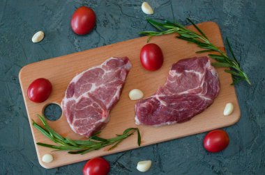 Domatesli çiğ domuz bifteği, sarımsak ve biberiye ahşap kesim tahtasının üstünde.