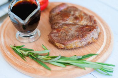 Pişmiş, ahşap bir tahtanın üzerinde ızgara domuz eti, soya sosu, biberiye ve domates, açık arkaplanda.