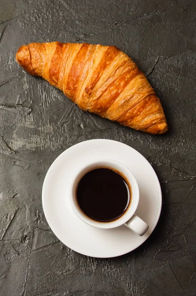 Café en una taza blanca y croissant sobre fondo de hormigón oscuro, vista superior, puesta plana. Concepto para el desayuno, la pausa para café o el almuerzo de negocios. Formato de marco vertical — Foto de Stock