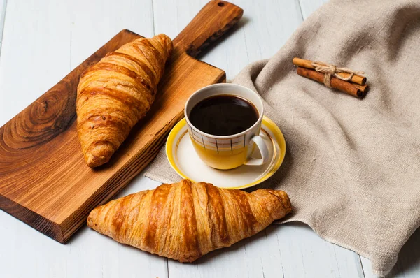 Café en tasse et soucoupe jaune vintage et croissants sur une assiette en bois, serviette en lin, sur fond clair, un concept de petit déjeuner rustique — Photo