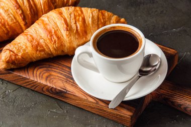 Kahve, ristreto ya da espresso ve kruvasan. Koyu arkaplanda, ahşap bir tahta üzerinde. Yakın plan.