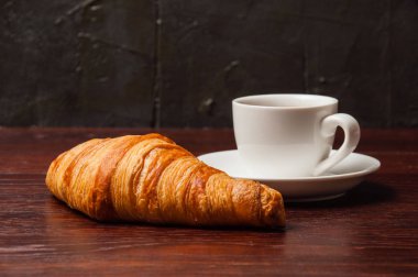 Lezzetli kahvaltı, bir fincan kahve ve koyu ahşap masa üstünde kruvasan.