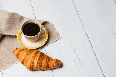 Klasik sarı bardakta espresso, çay tabağı ve kaşık, keten peçeteli kruvasan, hafif arka plan, öğle yemeği konsepti.