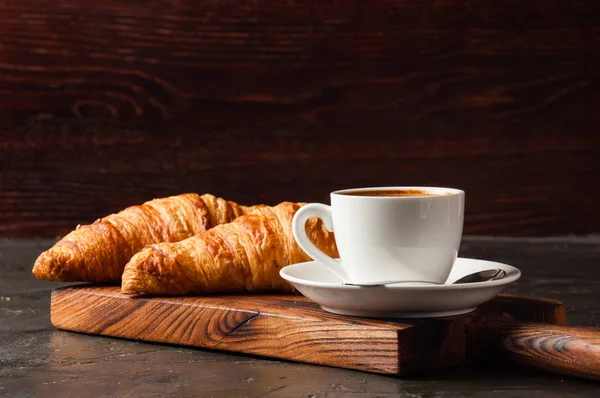 Espresso dans une tasse blanche et deux croissants sur fond sombre, sur une planche en bois, endroit pour le texte, vue latérale — Photo