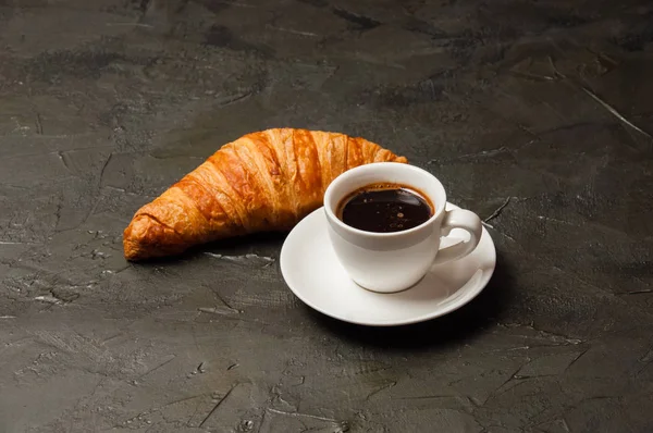 Café en taza blanca y un croissant sobre un fondo de hormigón oscuro, vista desde la parte superior, hay un lugar para el texto. Concepto desayuno, pausa para café o almuerzo de negocios — Foto de Stock