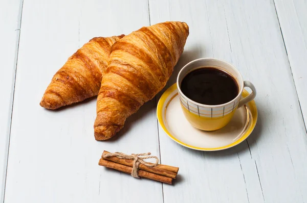 Café expresso en tasse jaune vintage, croissants et cannelle sur fond clair, concept petit déjeuner — Photo