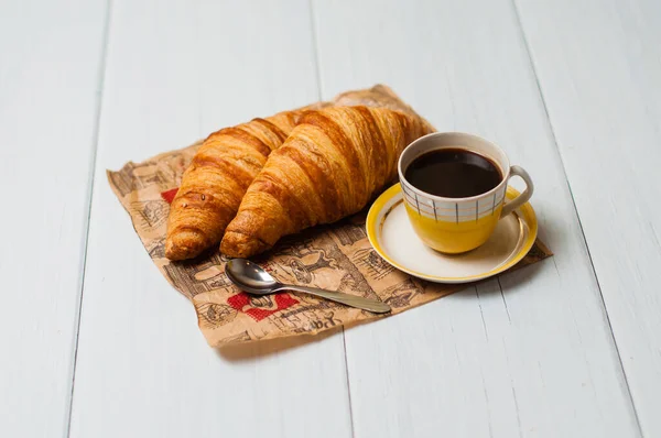 Café expresso dans une tasse jaune vintage avec une soucoupe et une cuillère, croissants sur papier artisanal, sur un fond clair, concept petit déjeuner — Photo