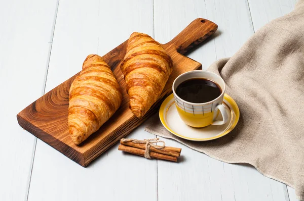 Café em xícara amarela vintage e pires e croissants em uma placa de madeira, guardanapo de linho, em fundo claro, um conceito de café da manhã rústico — Fotografia de Stock