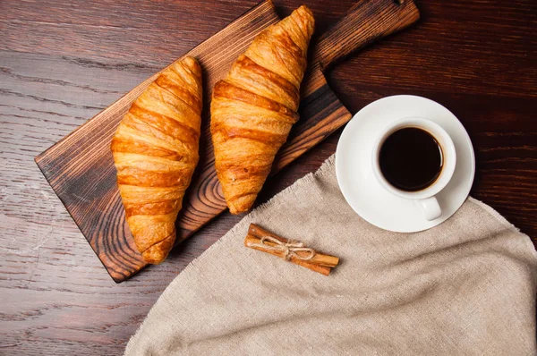 Concept délicieux petit déjeuner. Croissants à la cannelle, tasse de café et une serviette en lin sur une table en bois, vue sur le dessus, plat — Photo