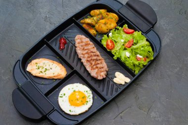 Kahvaltı, biftek ya da pirzola, domatesli ve yeşil sebzeli salata, tost, patates, siyah tabakta yumurta. Sağlıklı beslenme, diyet, menü, yüksek kalite öğle yemeği konsepti.