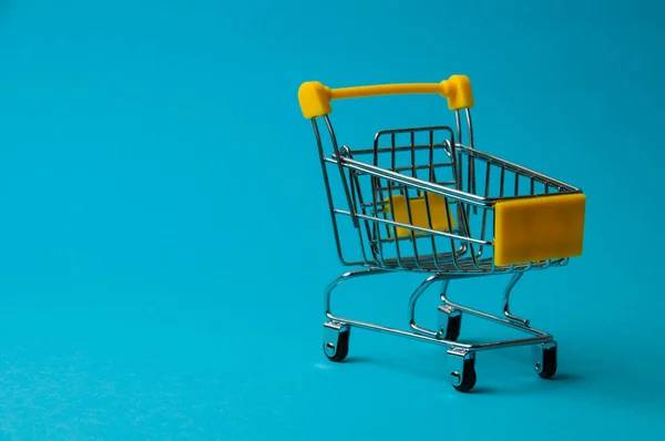 Trolley for shopping on blue background. Supermarket food price concept, holiday discounts