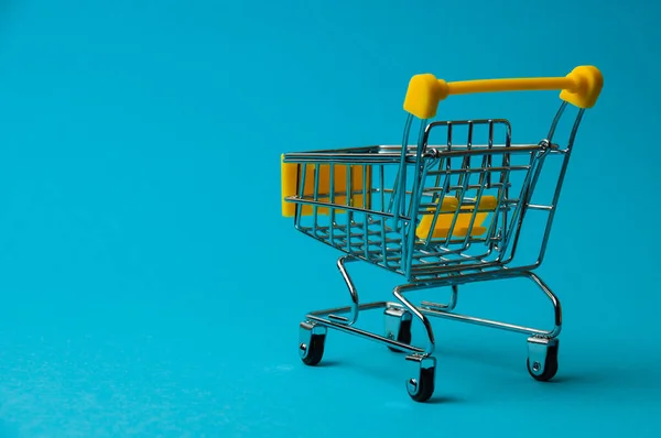 Trolley for shopping on blue background. Supermarket food price concept, holiday discounts