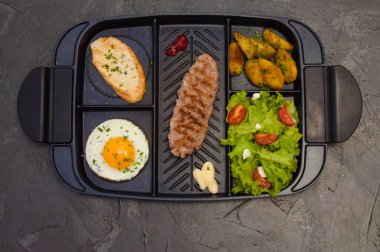 Kahvaltı, biftek ya da pirzola, domatesli ve yeşil sebzeli salata, tost, patates, siyah tabakta yumurta. Sağlıklı beslenme, diyet, menü, iyi beslenme.