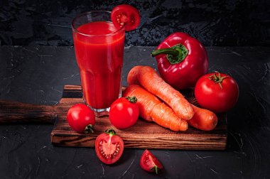 Bardaktaki sebze suyu ve kesme tahtasındaki sebzeler: havuç, biber ve domates.