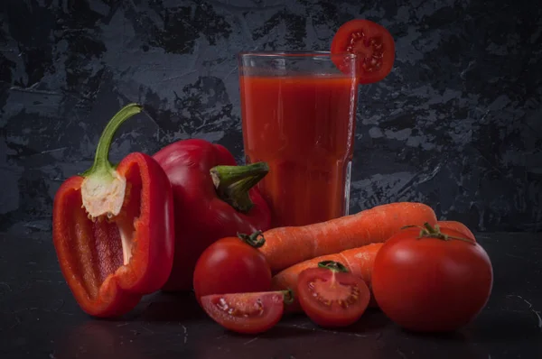 Warzywa marchew, pomidor i papryka w plasterkach, ze szklanką soku na powierzchni ciemnego betonu — Zdjęcie stockowe