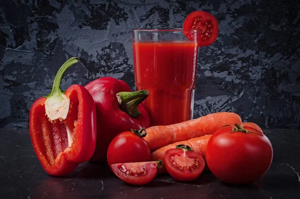 Gemüsekarotten, Tomaten und Paprikascheiben mit einem Glas Saft auf einer dunklen Betonoberfläche — Stockfoto