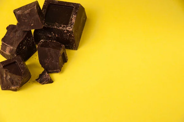 Pedaços apetitosos de chocolate preto isolado em um fundo amarelo close-up, espaço de cópia da direita — Fotografia de Stock