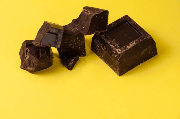 Pedaços apetitosos de chocolate preto isolado em um fundo amarelo close-up, espaço de cópia a partir do fundo — Fotografia de Stock