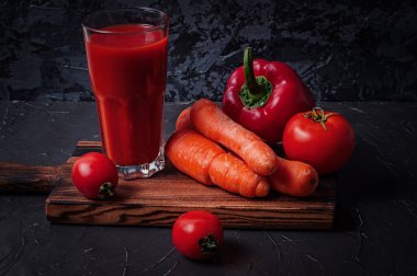 Bardaktaki sebze suyu ve aktüt tahtasındaki sebzeler: havuç, biber ve domates.