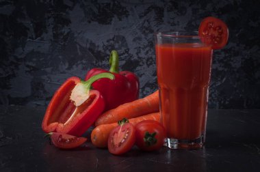 Sebzeler, havuç, domates ve koyu beton yüzeyde bir bardak meyve suyu ile dilimlenmiş biber.