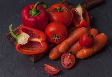 Sebze havucu, domates, biber dilimlenmiş mutfak tahtası, koyu beton yüzey, üst manzara.