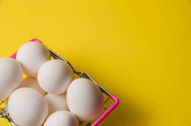 Sarı arka planda metal market sepeti içinde tavuk yumurtası.