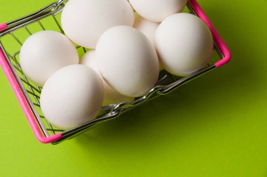 Neon yeşil arka planda metal market sepeti içinde yumurtalar.