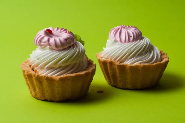 Two delicious pastries with cream on green background