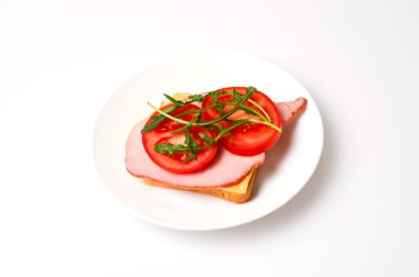 Beyaz bir tabakta sandviç, peynir, ekmek, domates ve roka.