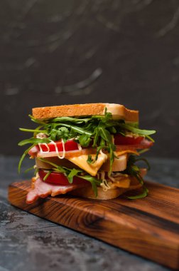 Jambonlu, balyklı, roka, peynirli, domatesli ve mayonezli büyük lezzetli sandviç. Köy usulü, arka planda gri bir görünüm var. Boşluğu kopyala.