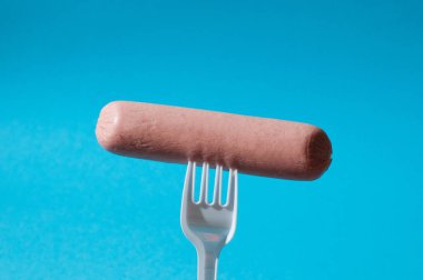 Mavi arka planda plastik çatallı çiğ sosis.