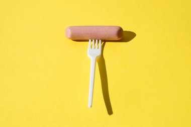 Sosis ve beyaz plastik çatal parlak sarı arka planda sert ışıkla