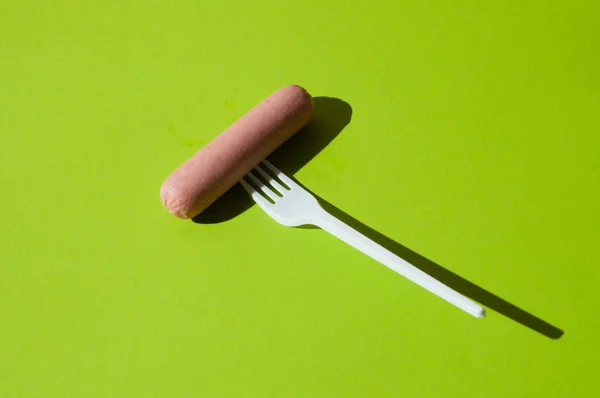 绿色背景下的香肠和塑料叉子 — 图库照片