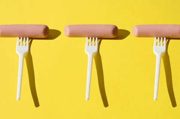 Fantasia, salsicce crude e forchette di plastica su fondo giallo brillante — Foto Stock