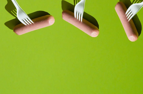 Patrón, varias salchichas crudas y tenedores de plástico sobre un fondo verde, espacio de copia — Foto de Stock
