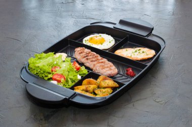 Kahvaltı, pirzola ya da biftek, domates salatası, kızarmış patates, kızarmış ekmek ve siyah tabakta kızarmış yumurta. Restoran yemeği, site için içerik