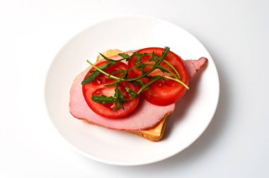 Balyk sandviçi, peynir, ekmek, domates ve roka beyaz bir tabakta