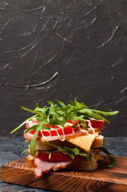 Çok iştah açıcı büyük bir sandviç jambon veya balyk, roka, peynir, domates ve mayonez ile kesme tahtasının üzerinde kırsal tarzda gri arka plan görünümlü, boşluk kopyala