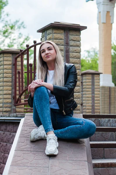Siyah deri ceketli, baharda verandada, güzel bir evin yanında kot pantolonlu tatlı, pozitif sarışın kız.