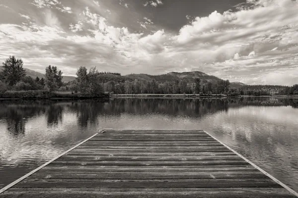 B&W of wood dock by calm river. — Stock Photo, Image