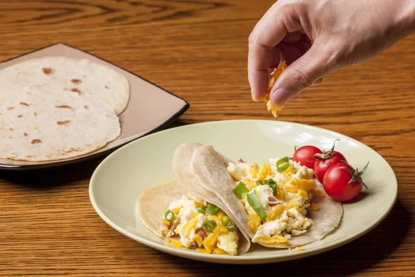 Sprinkling cheese on breakfast burritos. — Stock Photo, Image