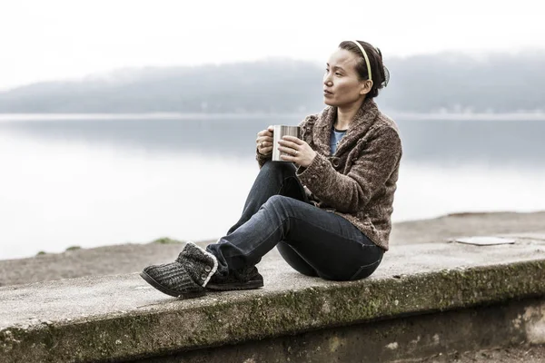 Frau sitzt auf Felsvorsprung am See. — Stockfoto