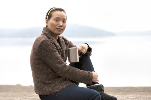 Asian woman enjoys coffee by lake. — Stock Photo, Image