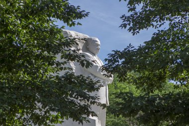 Ağaçların arasında görülen Mlk heykeli.
