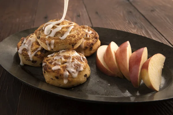 Frosting poured on cinnamon rolls with apple slices. — Stock Photo, Image